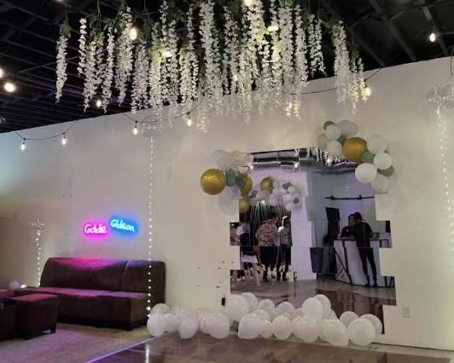 The image shows a decorated event space with a mirrored wall feature, balloons, string lights, and a neon sign reading "Gold & Gibbon."