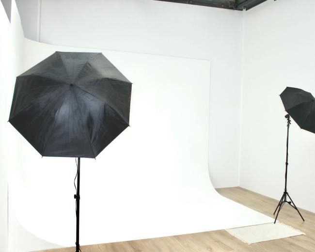 A photography studio with two black umbrellas on stands, illuminating a seamless white backdrop.