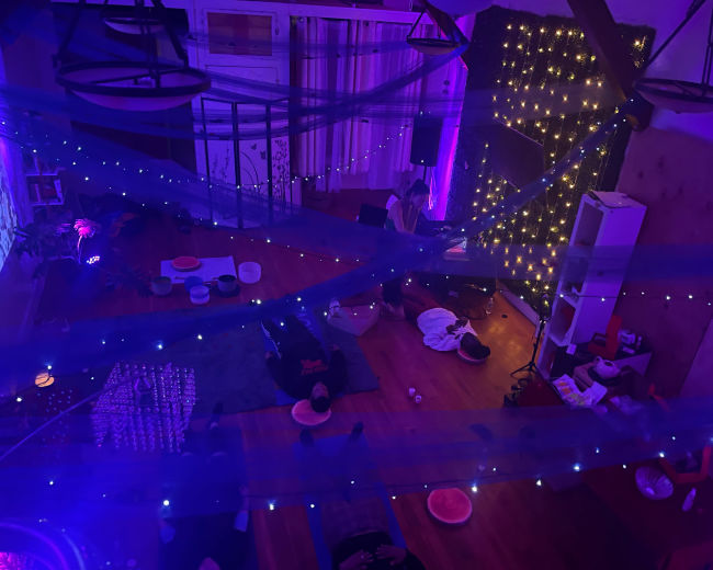 A multi-purpose indoor space with soft lighting, decorative string lights, and people sitting on the floor among mats and cushions.