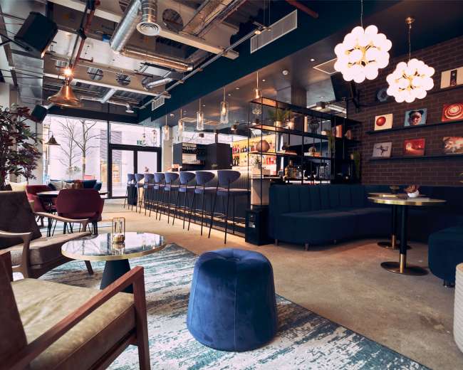 The image shows a modern café interior with a bar area, seating arrangements, and stylish lighting fixtures.