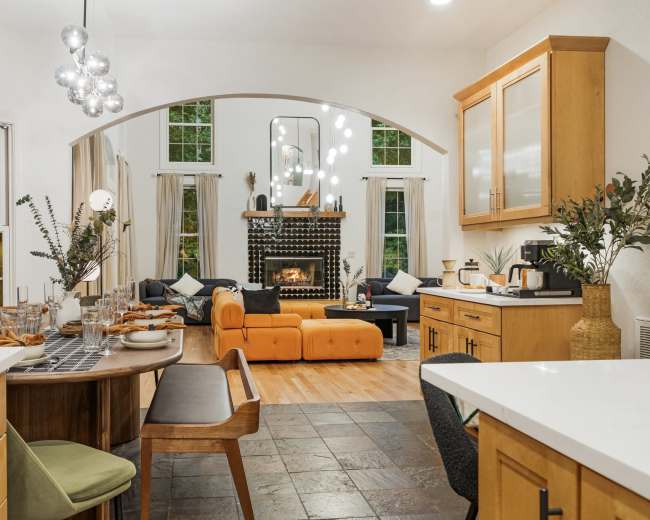 A modern kitchen opens up to a cozy living area featuring a fireplace, large windows, and contemporary furniture.