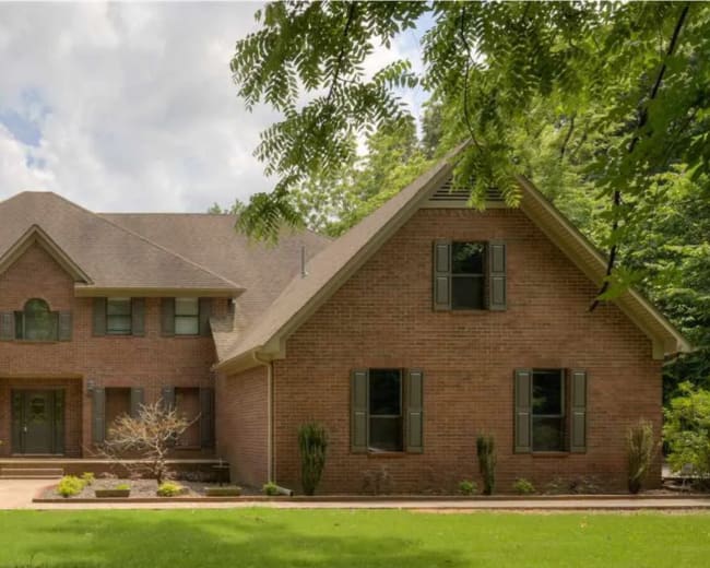 A large two-story brick house with a landscaped front yard and a mixture of symmetrical and asymmetrical architectural features.