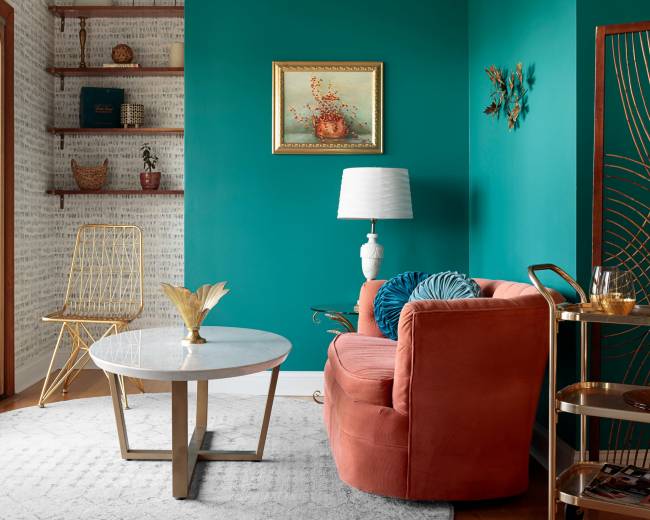 A cozy living room features a coral velvet sofa, a marble coffee table, and a turquoise wall with a potted plant on a shelf.