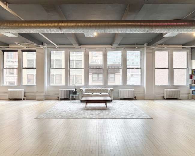 The scene shows a spacious, modern room with large windows, a white couch, and a coffee table on a light-colored rug.