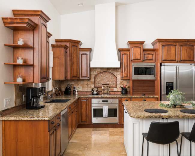 The image shows a kitchen with wooden cabinets, granite countertops, stainless steel appliances, and a center island with bar stools.
