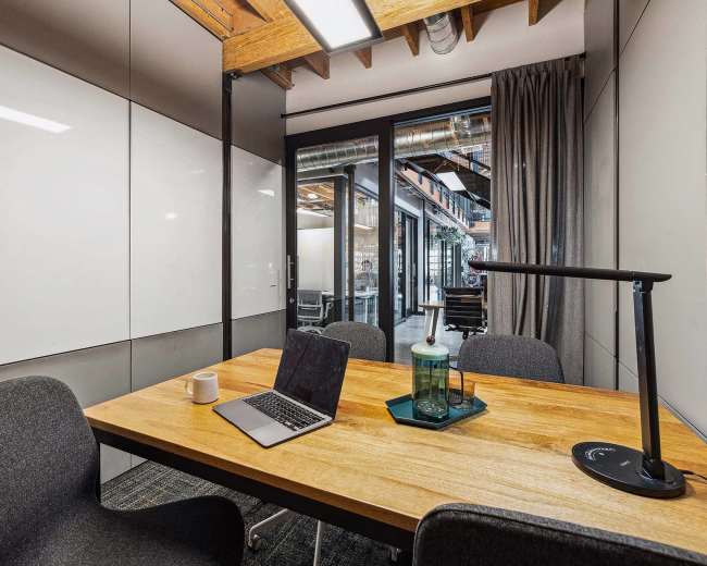 A modern conference room features a wooden table with a laptop, mug, and a decorative tray, surrounded by four chairs.