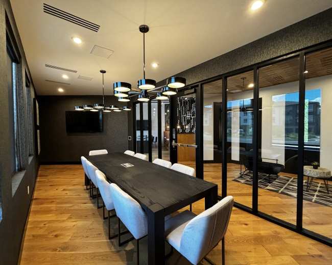 The image shows a modern conference room with a long black table, eight light-colored chairs, and large glass windows, featuring contemporary lighting fixtures and wooden floors.