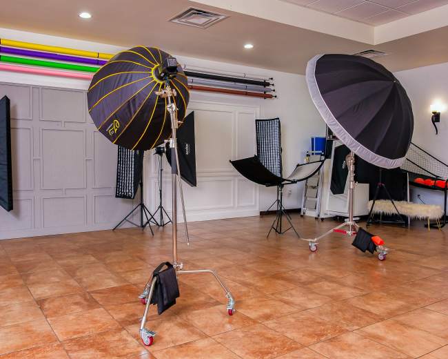 The image shows a photography studio equipped with various lighting setups, backdrop stands, and props arranged in a spacious interior.