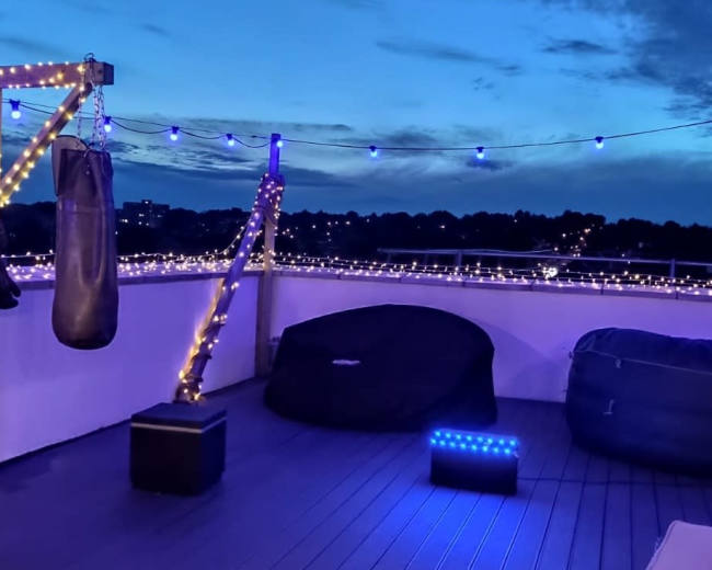 A rooftop area features a punching bag, seating, and string lights against a twilight sky.