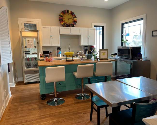 A modern kitchen with a central island, bar stools, stainless steel appliances, and a table with chairs arranged nearby.
