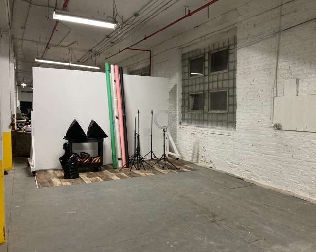 A studio space with blank backdrops, lighting equipment, and a wooden floor in a warehouse-like setting.