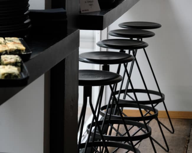 A countertop displays an assortment of colorful salads and small dishes alongside black plates and stools.