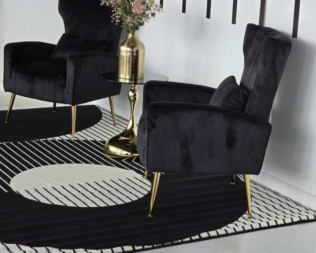 The image features two black velvet armchairs with gold legs flanking a small round table topped with a vase of flowers, set against a wall with vertical black stripes.