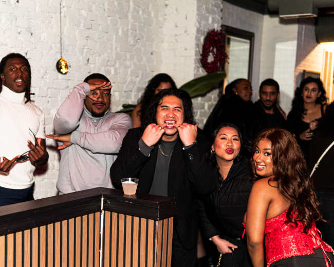 A group of people poses playfully in a social setting, with some making various gestures and facial expressions.