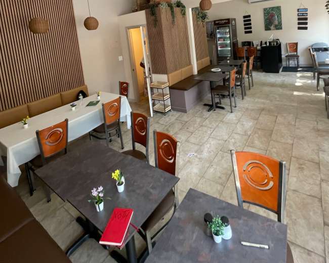 The image shows the interior of a restaurant featuring wooden paneling, tables with flowers, and a cash register area in the background.