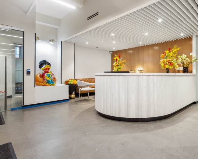 The image shows a modern reception area with a curved front desk, colorful floral arrangements, and a decorative statue in a corner.