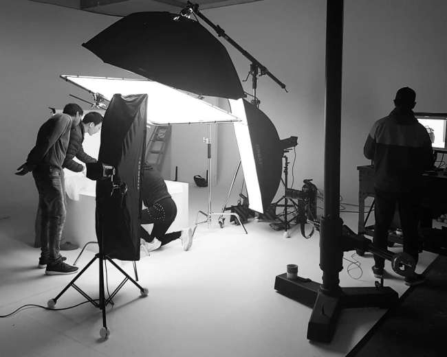 A photography studio setup is shown with multiple light sources and a team working around a backdrop.