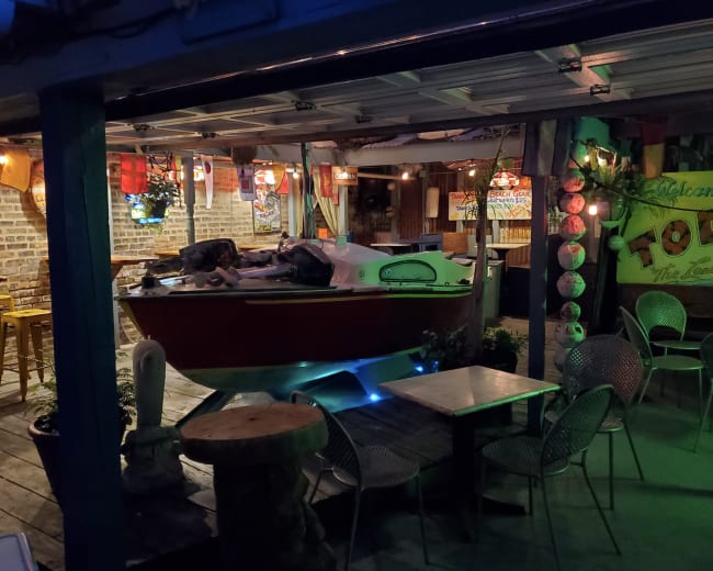 A small boat is displayed indoors in a rustic setting with tables and chairs arranged around it.