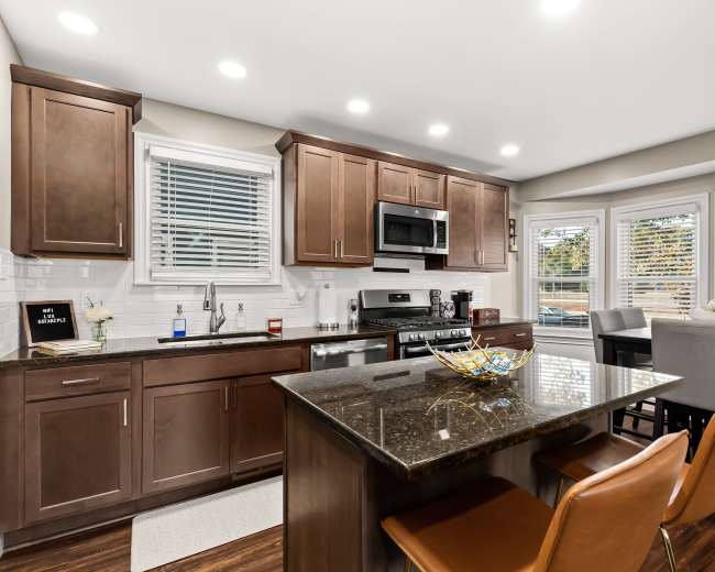 A modern kitchen features wooden cabinetry, stainless steel appliances, and a breakfast bar with two chairs.
