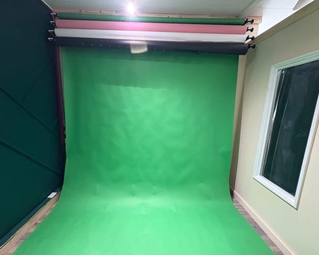 The image shows a green backdrop set up in a room with a white window on one side.