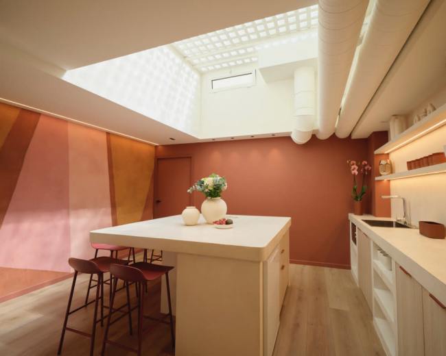 The image shows a modern kitchen featuring a central island, minimalist cabinetry, and large windows that allow natural light to flood the space.