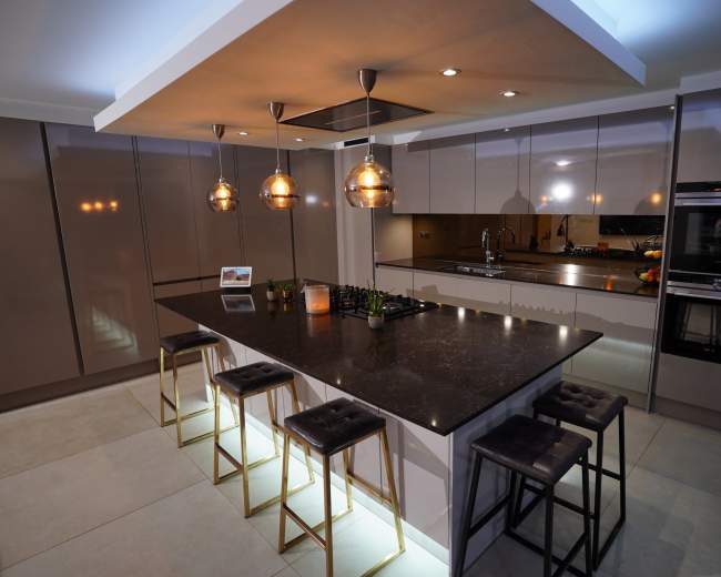 The image features a modern kitchen with a central island, sleek cabinetry, pendant lighting, and bar stools.