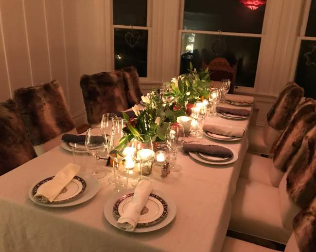 A long dining table is set with white tablecloths, plates, glassware, and candles, surrounded by chairs with fur covers.