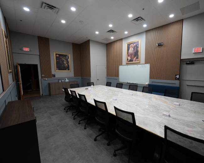 A spacious conference room features a large marble table surrounded by black chairs, with wall art and a whiteboard visible.