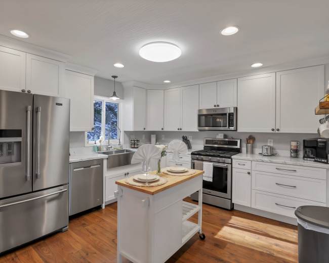 The image shows a modern kitchen with stainless steel appliances, white cabinetry, and a central wooden island.