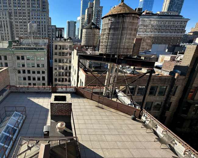 The image shows a rooftop view of a cityscape featuring several buildings, water towers, and a clear blue sky.