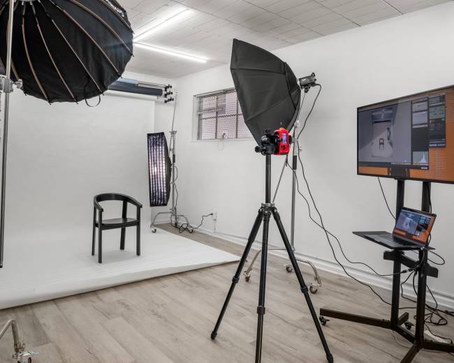 The image shows a photography studio equipped with lights, a backdrop, a chair, and a computer on a stand.