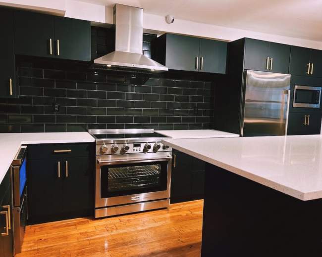 The image shows a modern kitchen with black cabinets, stainless steel appliances, and a white countertop.