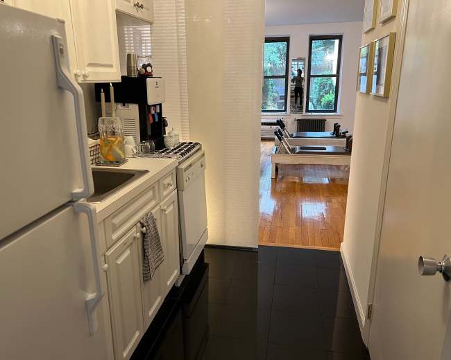 A compact kitchen with white cabinetry and a view into a living space featuring hardwood floors and large windows.