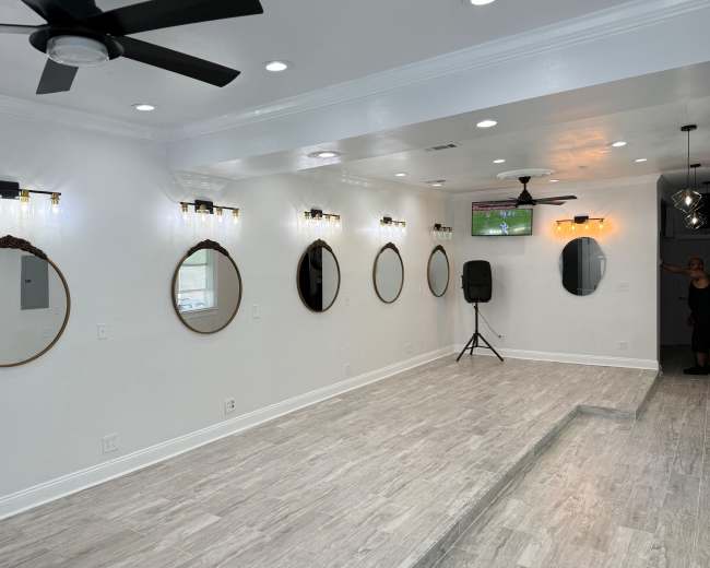 The image shows a modern, brightly lit room with multiple round mirrors mounted on the walls, a speaker in the corner, and a person standing near the back.