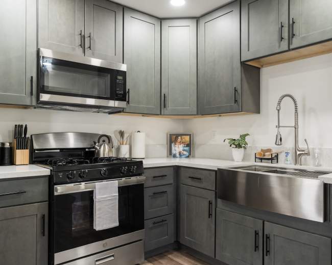 A modern kitchen featuring dark cabinetry, stainless steel appliances, and a farmhouse sink.