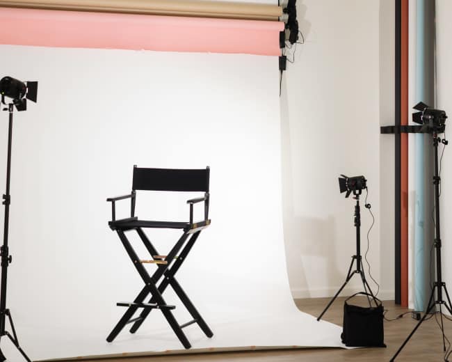A director's chair is positioned in front of a white backdrop, illuminated by studio lights on either side.