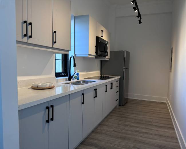 A modern kitchen with light-colored cabinetry, a stainless steel microwave and refrigerator, and a sink under a window.