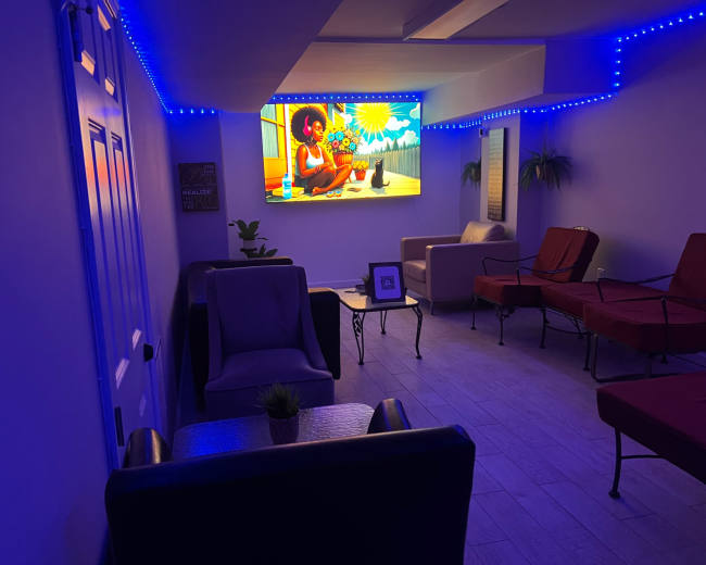 A cozy, modern lounge area features a vibrant digital screen displaying animated artwork, surrounded by comfortable seating and ambient lighting.