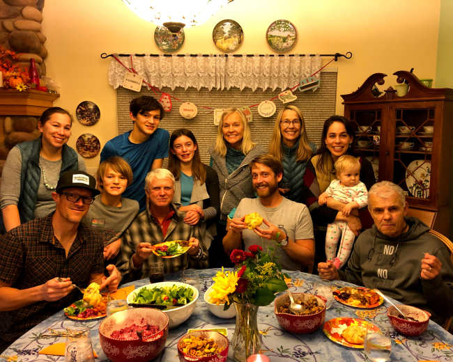A large group of people gathers around a dining table filled with food, smiling and enjoying a meal together.