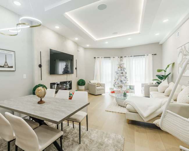 The image shows a modern living space with a dining area, a large television mounted on the wall, and a decorated Christmas tree in the corner.