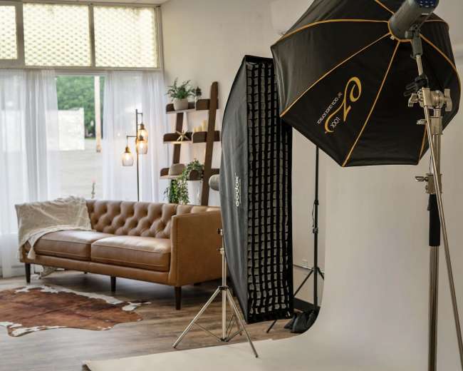 A photography studio setup with a brown leather couch, a backdrop, and lighting equipment in a softly lit room.