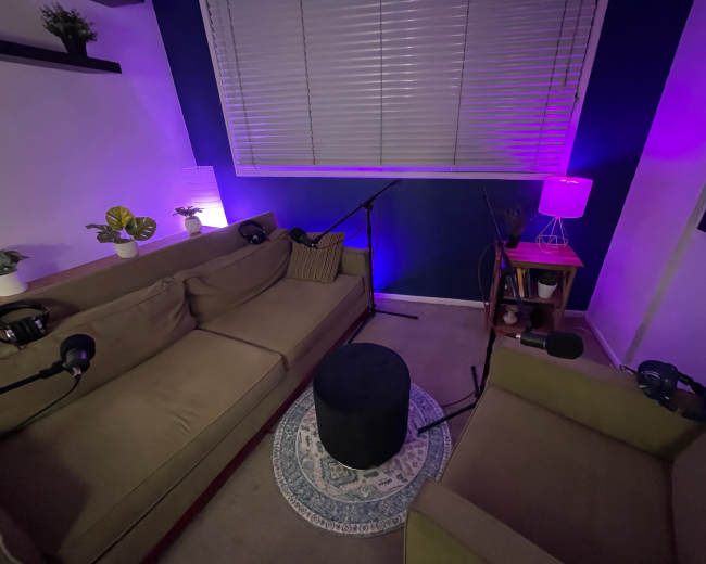A small recording studio is set up with two couches, microphones, and ambient lighting.