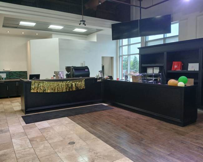 The image shows a dark wooden reception area with a counter, a coffee machine, and festive decorations, including a gold fringe, in a well-lit space.
