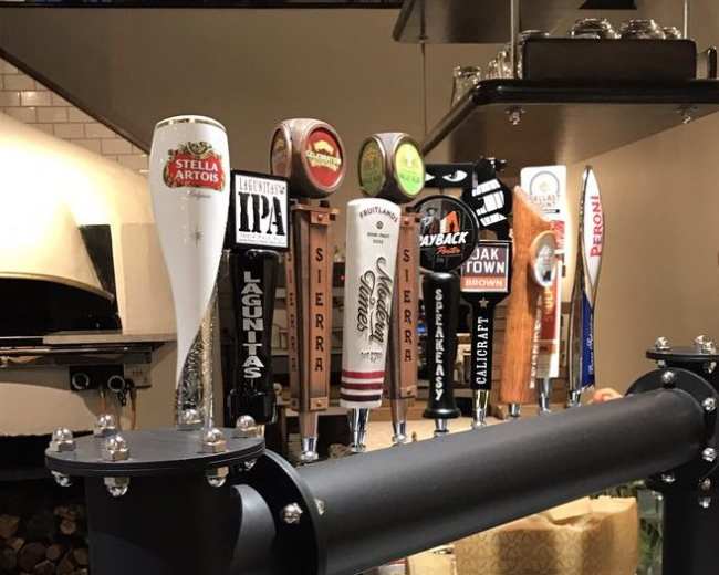 The image shows a row of various beer taps mounted on a black metal bar.
