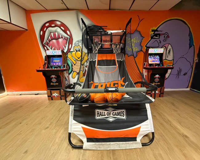 The image shows an indoor arcade featuring a basketball shooting game with colorful murals on the walls.