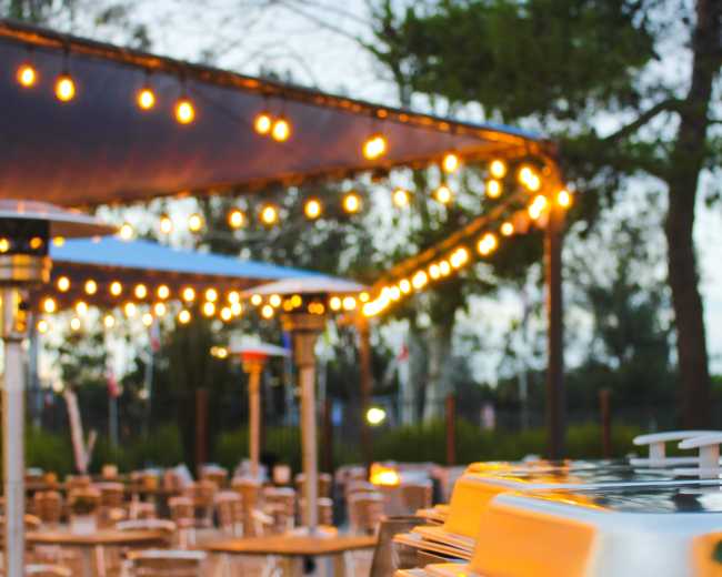 An outdoor dining area is illuminated by string lights, featuring tables and chairs arranged under a canopy.