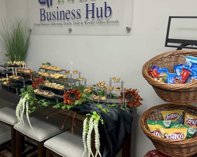 A buffet table with assorted appetizers and snacks is set up against a wall displaying a sign for "Business Hub."