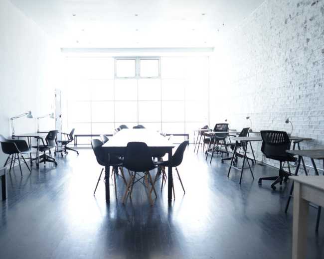 A spacious, minimalist office with a long table surrounded by black chairs and several workstations along the walls.