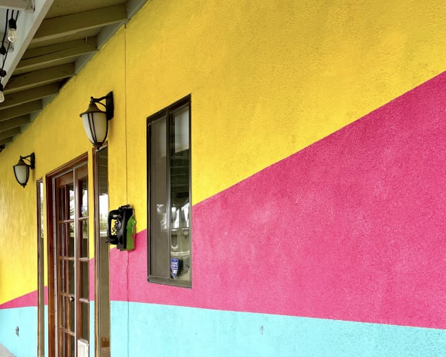 The image shows a brightly colored wall featuring yellow, pink, and aqua stripes, with a wooden door and light fixtures.