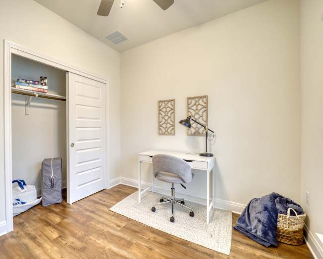 The image shows a minimalistic room featuring a desk and chair, a small closet, and hardwood flooring.
